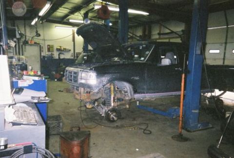 1994 Ford F-150 - A black Ford truck is on a lift in a garage, with its hood open and front end disassembled for repairs.