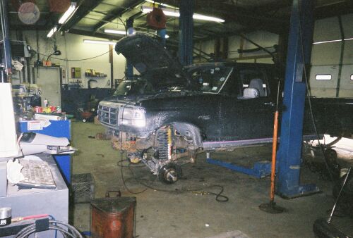 Black Ford truck with hood open, undergoing repairs on a lift. Front grille and headlights are visible
