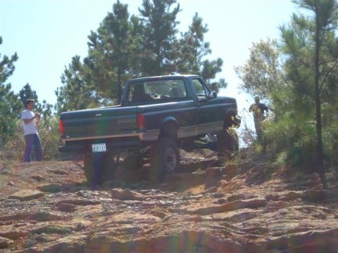 2008 International School Bus - A lifted Ford pickup truck navigates a challenging rocky terrain on a sunny day.