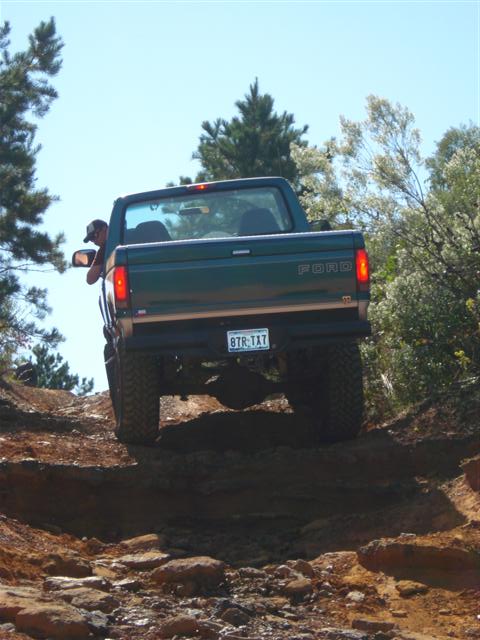 2008 International School Bus - A Ford pickup truck navigates a challenging off-road trail under a clear blue sky.