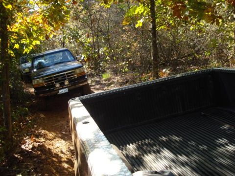 2008 International School Bus - Two trucks navigate a wooded trail, with one truck's bed prominently in the foreground.