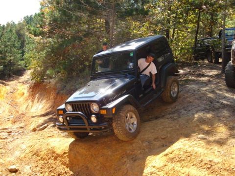 2008 International School Bus - A black Jeep Wrangler Rubicon navigates a challenging dirt trail, with other vehicles visible in the background.