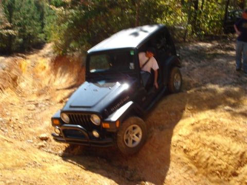 2008 International School Bus - Jeep Wrangler Rubicon navigating an off-road trail with a driver inside and another person observing.