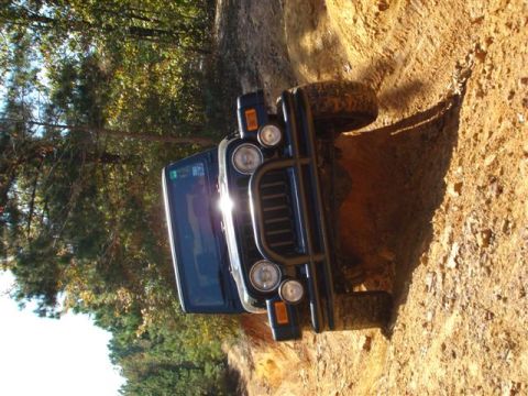 2008 International School Bus - A black Jeep Wrangler navigates a steep, muddy incline on a wooded trail.