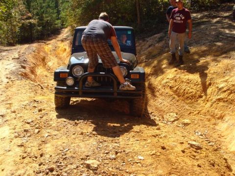 2008 International School Bus - A black Jeep Wrangler navigates a challenging dirt trail with a person standing on its hood.