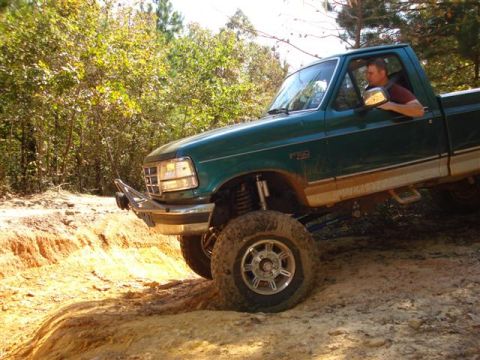 2008 International School Bus - A man drives a green Ford F-150 pickup truck off-road through a wooded area.