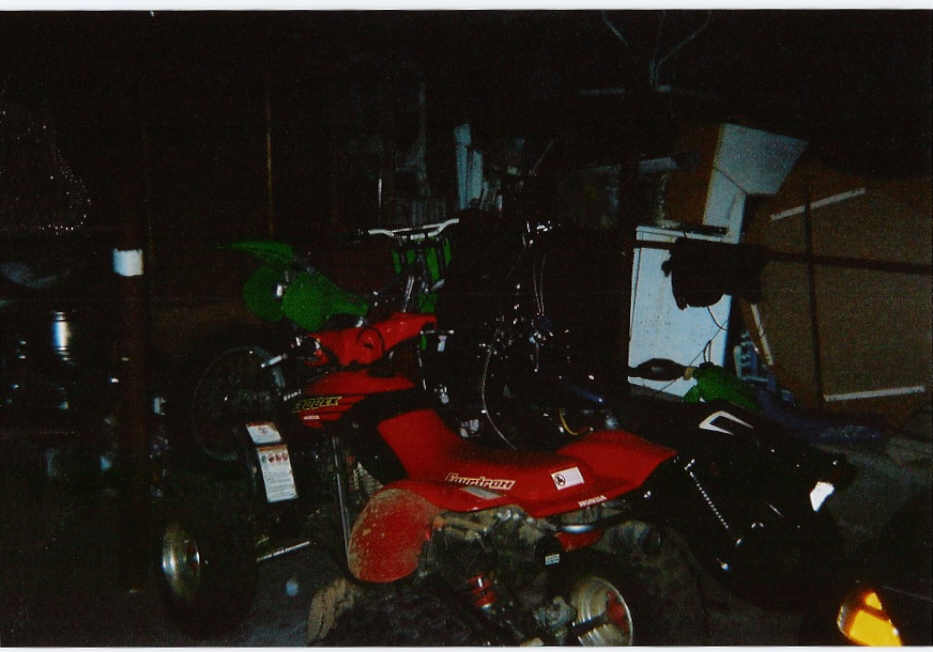 Red ATV and green dirt bikes crowded together in a dark cluttered garage