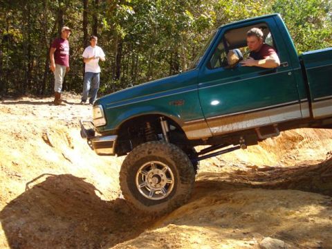2008 International School Bus - A green pickup truck navigates a challenging dirt path with two onlookers in the background.