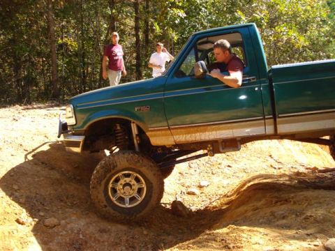 2008 International School Bus - A green pickup truck is shown off-roading on a dirt trail with two people standing in the background.
