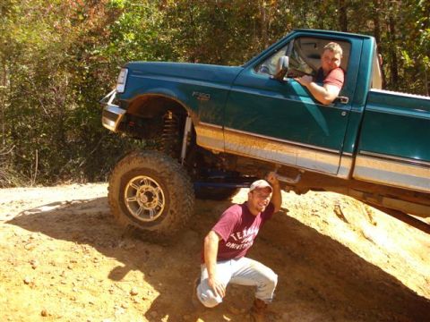 2008 International School Bus - A lifted green Ford F-150 is shown off-roading with two people inside and one posing underneath.