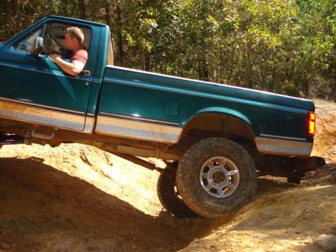 2008 International School Bus - A green pickup truck navigates a steep dirt incline in a wooded area.