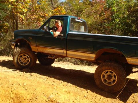 2008 International School Bus - A green pickup truck with a lifted suspension and large off-road tires navigates a dirt trail.