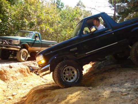 2008 International School Bus - Two trucks navigate a challenging dirt trail with steep inclines and loose soil.