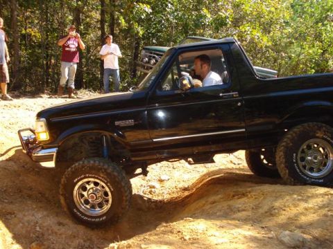 2008 International School Bus - A black Ford Bronco navigates a challenging off-road trail with spectators observing the action.