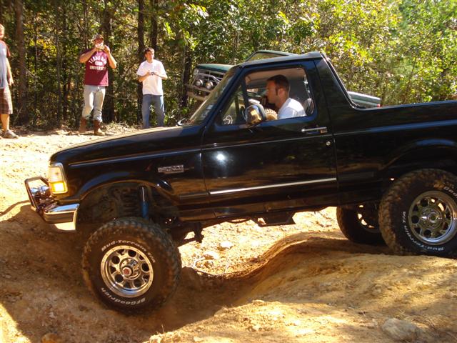 Black Ford Bronco driving on a dirt trail with people watching