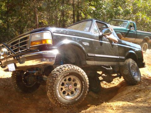 2008 International School Bus - A lifted black Ford Bronco navigates an off-road trail, with another pickup truck visible in the background.