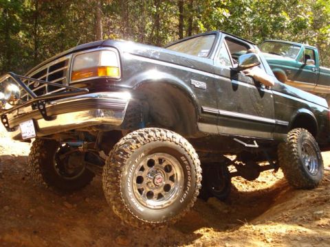 2008 International School Bus - A lifted black Ford Bronco navigates an off-road trail, with a green truck visible in the background.