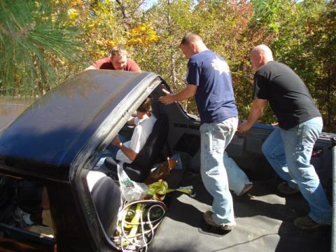 2008 International School Bus - Several men are pushing a black vehicle from the outside, with trees in the background.