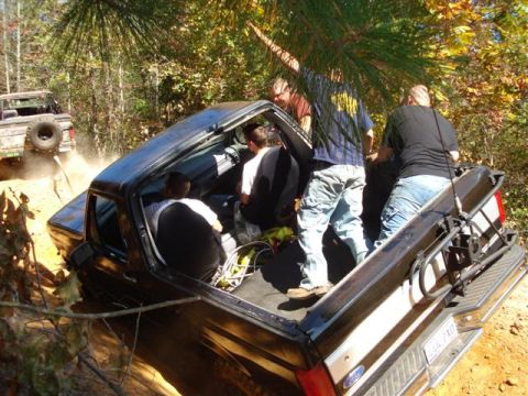 2008 International School Bus - A group of people are riding in the bed of a black pickup truck as another vehicle kicks up dust behind them on a dirt path.