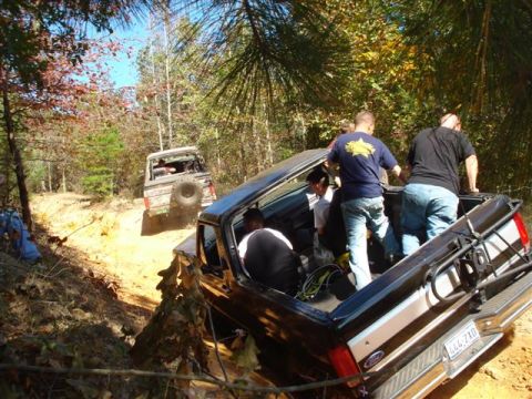 2008 International School Bus - Off-road trucks are seen on a dirt trail in a wooded area with people in the back of one.