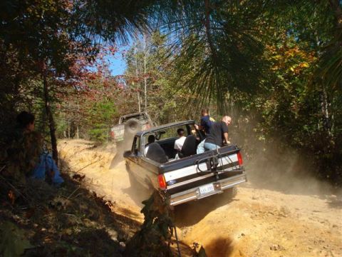 2008 International School Bus - People ride in the back of a truck as it kicks up dust on a wooded trail.
