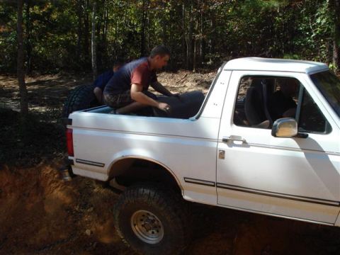 2008 International School Bus - People are loading items into the bed of a white pickup truck while off-roading.