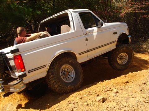 2008 International School Bus - A white lifted pickup truck navigates a steep dirt trail during an off-road excursion.