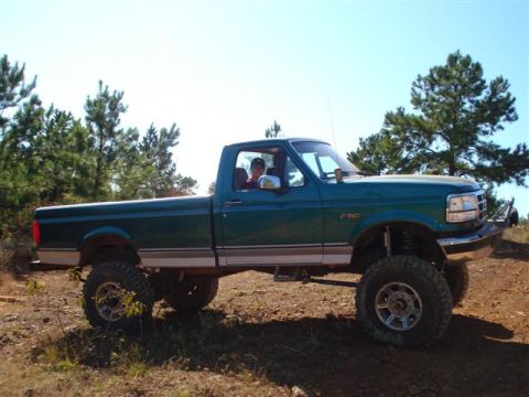 2008 International School Bus - A green pickup truck with a lifted suspension and large off-road tires is driven on a dirt path.