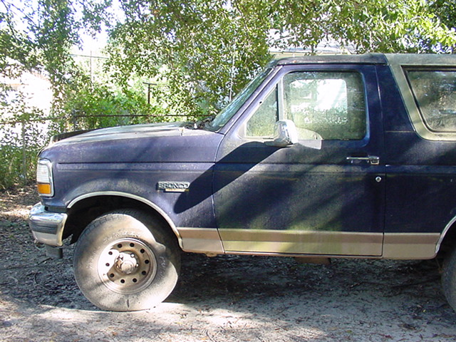Side view of a blue 1994 Ford Bronco with a flat tire and tan trim