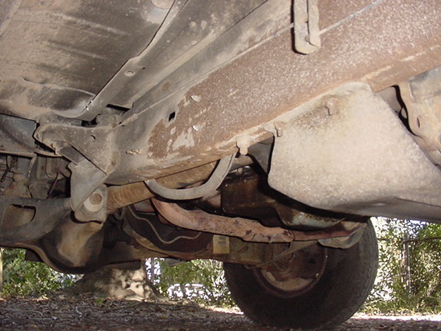 1994 Ford Bronco undercarriage, showing rusty frame rails, suspension components, and a rear tire