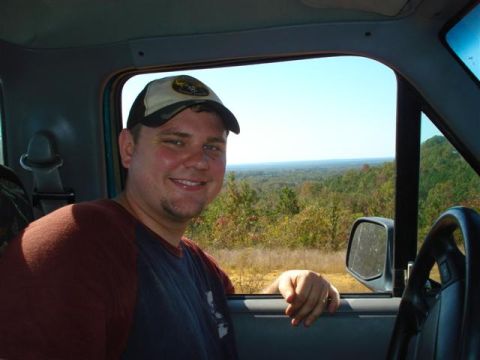 2008 International School Bus - A man smiles from inside a vehicle, with a view of rolling hills and trees outside the window.