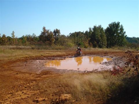 2008 International School Bus - A dirt bike rider navigates through a large muddy puddle in an outdoor, wooded area.