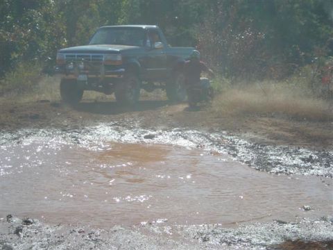 2008 International School Bus - A pickup truck navigates a muddy terrain, kicking up dirt as an ATV is visible in the background.