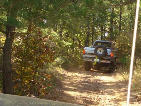2008 International School Bus - A white 1992 pickup truck navigates a wooded trail, its spare tire prominently displayed on the rear.