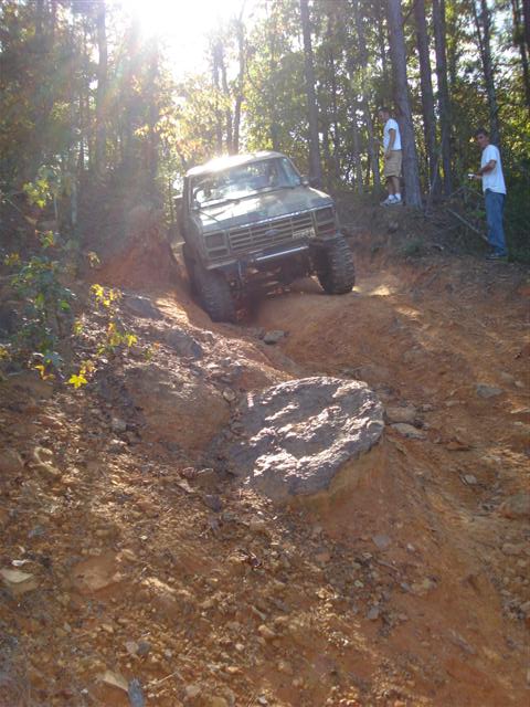2008 International School Bus - A modified pickup truck navigates a challenging off-road course with steep inclines and large rocks.