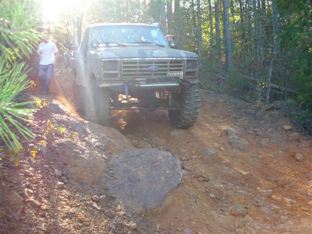 Green Ford F-Series truck with lifted suspension and off-road tires navigating a rocky incline