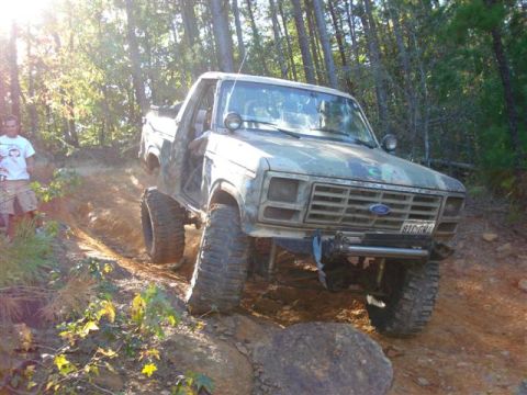 2008 International School Bus - Ford Bronco navigating an off-road trail with a person watching.