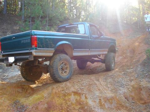 2008 International School Bus - A lifted green Ford pickup truck navigates a steep dirt trail, its off-road capabilities.