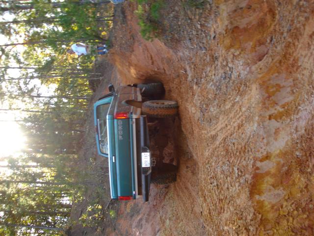 Green pickup truck with spare tire mounted on rear, driving on a dirt trail. License plate reads '978 TXX'