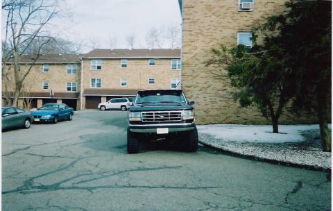 1994 Ford F-150 - A black Ford F-Series truck is parked in a lot with other vehicles and a brick building in the background.
