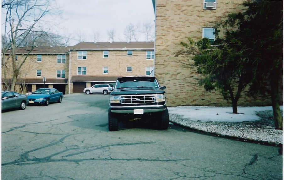 Front view of a black Ford F-Series truck parked in front of a brick building. Other cars are visible in the background