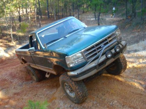 2008 International School Bus - This pickup truck is navigating a steep, muddy incline in a wooded area.