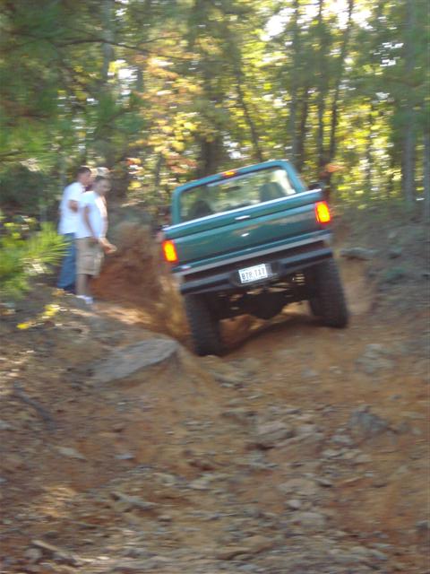 2008 International School Bus - A green pickup truck navigates a steep, rocky dirt trail with onlookers present.