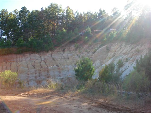 Two off-road vehicles on a dirt embankment with trees and a sunny sky