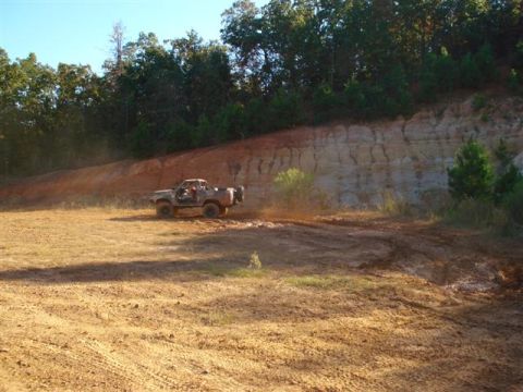 2008 International School Bus - A pickup truck navigates a dirt track in a wooded area with a sandy embankment.