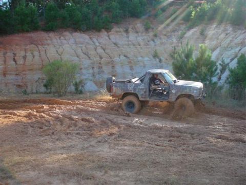 2008 International School Bus - A camouflaged pickup truck navigates a muddy off-road course with a steep dirt embankment behind it.