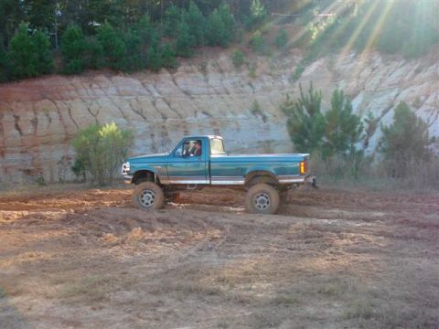 2008 International School Bus - A teal pickup truck navigates a muddy terrain with a dirt embankment in the background.