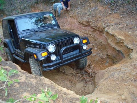 2008 International School Bus - A Jeep Wrangler navigates a challenging off-road obstacle, with a person sitting on the embankment above.