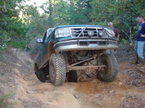 2008 International School Bus - A modified pickup truck navigates a steep, muddy incline on an off-road trail.