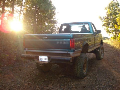 2008 International School Bus - A Ford pickup truck is seen from the rear on a dirt road with the sun setting behind it.